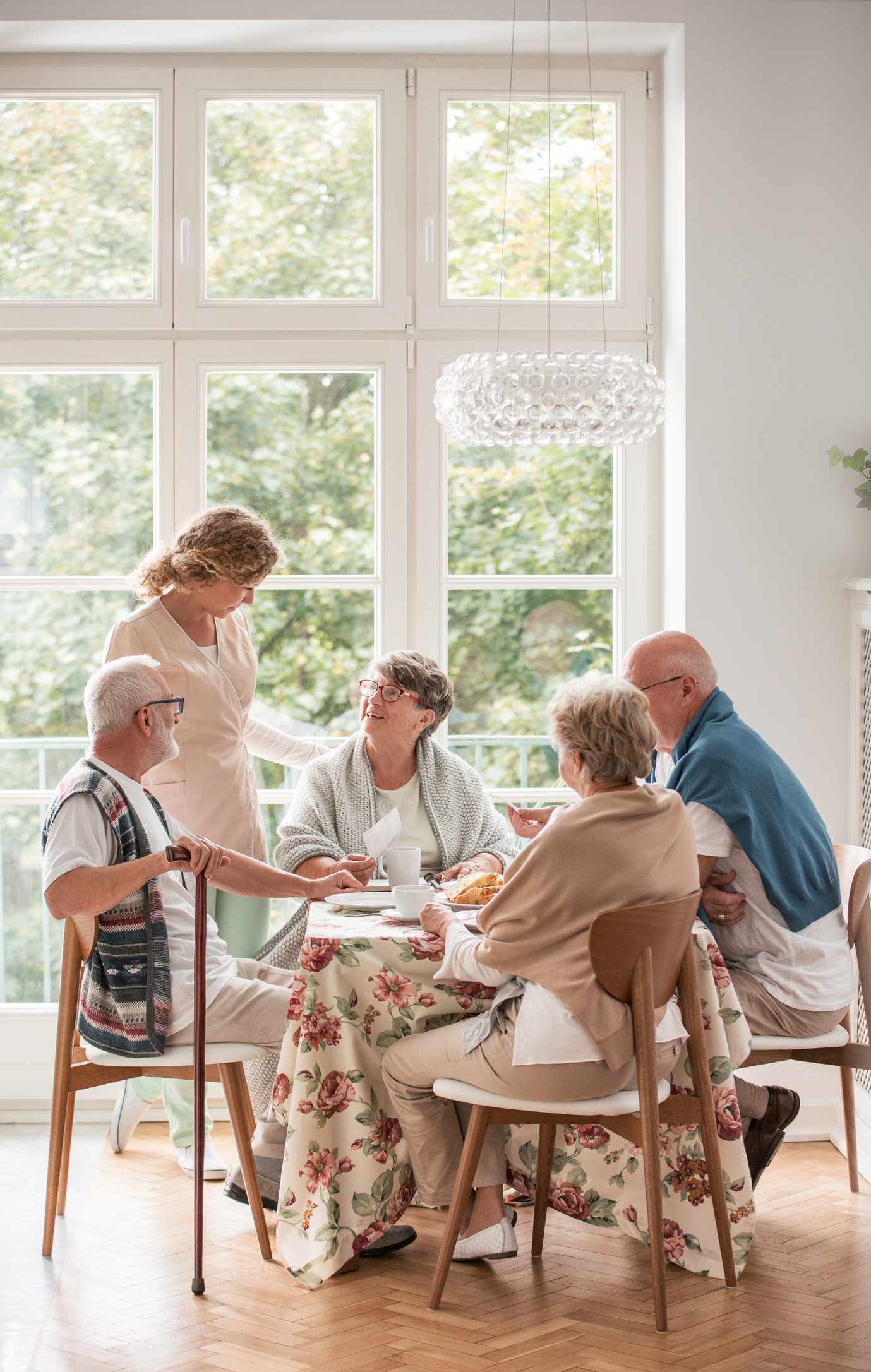 Elderly friends spending time together by drinking tea and enjoying photos in common dining room of nursing home Residents and care partner sharing time together in a residential memory care home near The Woodlands